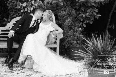 A picture taken in Reportage style of a Bride and Groom Kissing on a bench in black and white